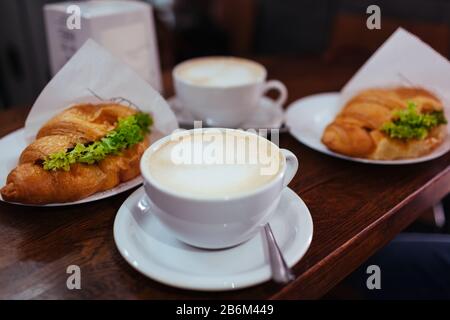 Croissant Sandwiches und Latte Kaffee auf dem Café-Tisch serviert. Frühstück mit frischen Backwaren und heißen Getränken Stockfoto
