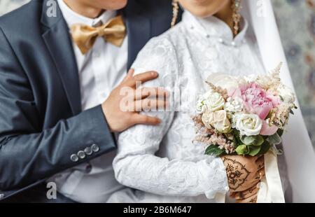 Das Brautpaar umarmt und hält einen Hochzeitstrauß aus Pastellblüten aus nächster Nähe Stockfoto