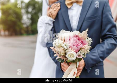 Das Brautpaar umarmt und hält einen Hochzeitstrauß aus Pastellblüten aus nächster Nähe Stockfoto
