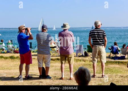 Vier ältere Männer in Shorts, T-Shirts und Hüten stehen mit dem Rücken zur Kamera und blicken auf einen sonnigen Tag. Stockfoto