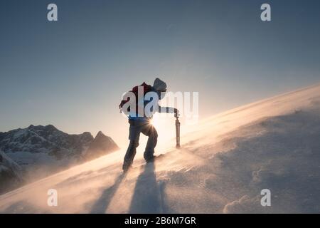 Der Fotograf mit Stativ klettert bei Sonnenuntergang auf einem Hügel am Ryten Mount in blizzard Stockfoto