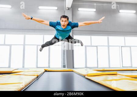 Ein junger Fit glücklicher Mann, der im Fitness-Fitnessstudio auf Trampolin springt und fliegt Stockfoto