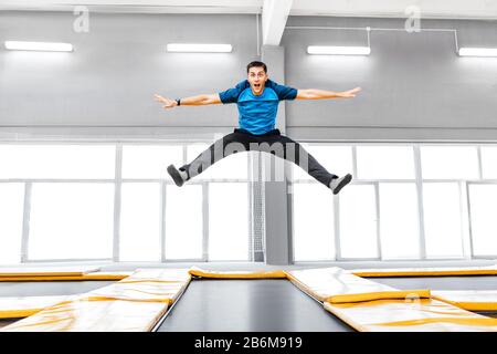 Ein junger Fit glücklicher Mann, der im Fitness-Fitnessstudio auf Trampolin springt und fliegt Stockfoto