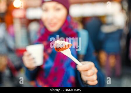 Frau isst Wurst mit heißem Wein auf dem zentralen Platz in der europäischen Stadt. Konzept der Straßennahrung im Winter in der Nähe von Touristenattraktionen Stockfoto