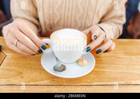 Weibliche Hände in Nahaufnahme und Cappuccino in weißer Tasse auf Holztisch Stockfoto