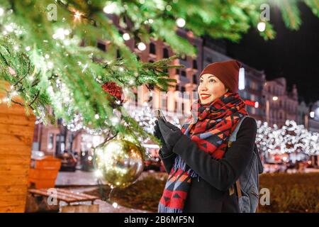 Nachts bewunderte die Touristin den Weihnachtsbaum mit Lichtern auf dem Hauptplatz der europäischen Stadt an Silvester Stockfoto