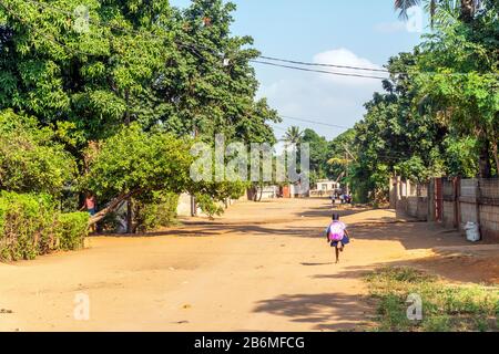 Afrikanisches Mädchen mit großem Rucksack auf Sandy Road zur Grundschule in Matola, Mosambik Stockfoto