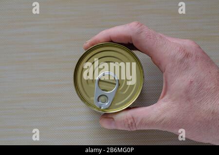 Die Hand eines erwachsenen Mannes hält eine Dose Konserven. Geschlossene Dose mit geöffnetem Schlüssel in der Hand. Die Hand eines Mannes hält eine Dose Konserven. Konserven. Diese REA Stockfoto