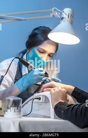 Eine Frau, die im Salon Maniküre meistt und dabei mit den Nägeln des Kunden auf blauem Hintergrund arbeitet. Kosmetologie und Nagelpflege Stockfoto