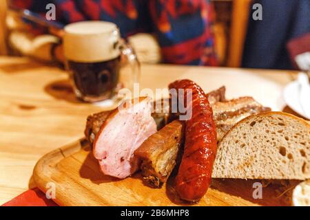 In der Bar oder im Restaurant wird der tschechische Becher mit Bier und traditioneller Wurst- und Schweinefleisch auf einem weißen Teller zubereitet Stockfoto