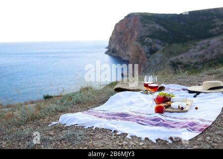 Ein romantisches Picknick mit Gläsern Wein mit Obst und Käse auf einer grünen Wiese an der felsigen Küste am Sommerabend Stockfoto