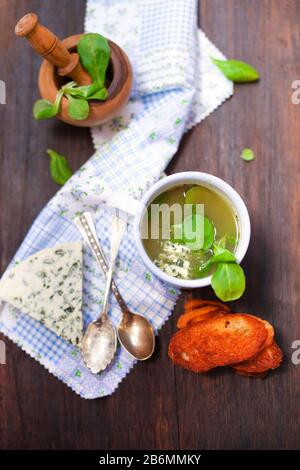 Blick auf köstliche Suppe in weißem Becher mit frischen Kräutern und Gorgonzola-Käse neben Mörtel und Pfirsiche auf Holztisch mit Toast Stockfoto