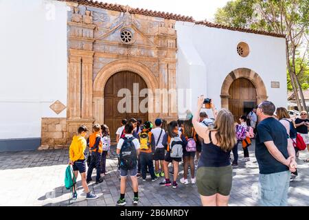 Eine Schulgruppe und Touristen, die die Schnitzerei mit aztekischen Einflüssen auf die Kirche von Iglesia Nuestra Senora de la Regla in Pajara an der Kanarischen Insel Bewundern Stockfoto