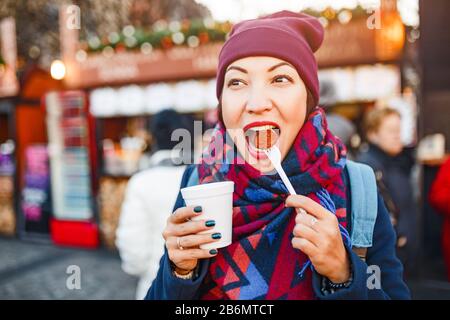 Junge Frau Reisender Snacks eine Wurst mit einem heißen Getränk auf der Straße einer europäischen Stadt im Winter Stockfoto
