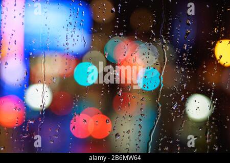 Bokeh Hintergrund der hellen Stadtlichter nachts durch ein schmutzig regnerisches Hotelfenster Stockfoto