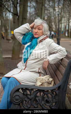 Eine elegante ältere grauhaarige Frau sitzt auf einer Parkbank. Stockfoto