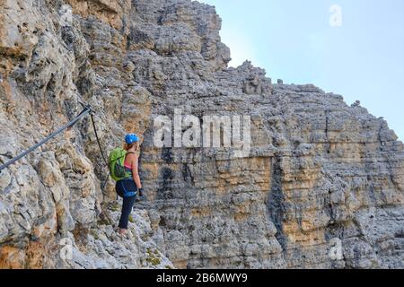 Frau auf der Via ferrata Cesare Piazzetta, mit Blick auf einen belichteten Abschnitt mit beeindruckenden Felswänden um ihn herum. Aktivurlaub in der Sella Gruppe, Dololi Stockfoto