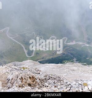 Kurvenreiche Straße im Nebel am Pass von Pordoi, Berge der Dolden, Italien. Blick von oben auf die Kletterroute Eterna Brigata Cadore. Stockfoto