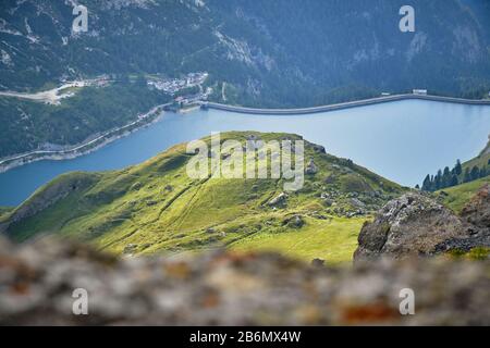 Sonnenflecken auf grünem Hügel über dem Fedaiasee in den Bergen der Dolinen, Italien, wie man von einer Wanderroute oben sieht. Stockfoto