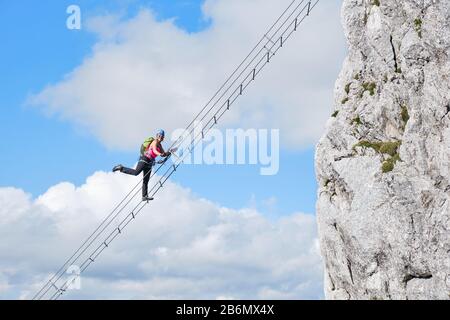 Touristin hebt ihr Bein auf der Kletterroute Intersport Klettersteig Donnerkogel in Österreich. Treppenaufgang zum Himmel Konzept. Stockfoto