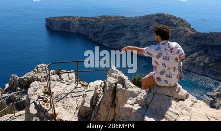 Männlicher Teenager, der von einer Klippe auf das Meer zeigt Stockfoto