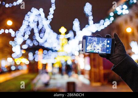 Prag, TSCHECHIEN - DEZEMBER 2017: Frau Fotografieren nachts den europäischen Weihnachtsmarkt mit Glühbirnen auf Dem Smartphone Stockfoto