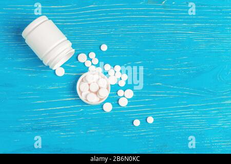 Weiße Pillen wurden aus einem weißen Behälter über blauem Holzhintergrund verschüttet Stockfoto