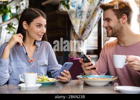 Attraktives junges Paar, das im Café zuhause zu Mittag essen und mit dem Handy eine Mahlzeit zu sich nehmen kann Stockfoto