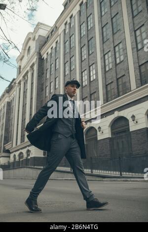 Ein Mann spaziert auf der Stadtstraße nach einem englischen Retro-Gangster der 1920er Jahre, der in Pekligen Schlinderstil gekleidet ist. Stockfoto