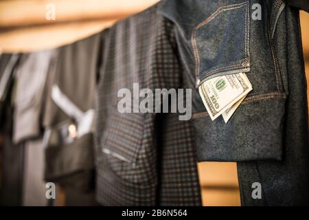 Dunkle, stylische Hosen und Jeans für Damen hängen an einem Seil in der garderobe, und Geldscheine fallen aus ihren Taschen. Das Konzept der Auswahl von c Stockfoto