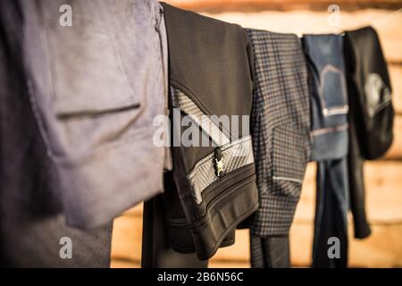 Dunkle, stylische Hosen und Jeans für Damen hängen an einem Seil in der garderobe. Das Konzept, Kleidung für jeden Tag zu wählen. Elegantes Damenbekleidungskonzept Stockfoto