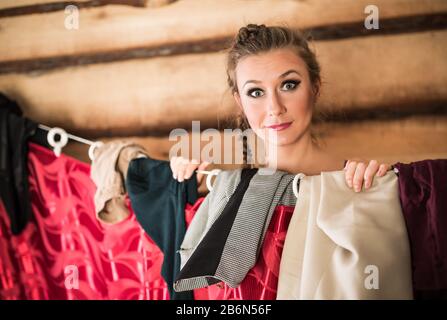 Charmantes lächelndes Mädchen reiht sich beim Ankleiden hinter die garderobe des roten Vorhanges. Verschiedene Kleidungskonzepte Stockfoto