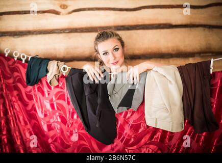 Charmantes lächelndes Mädchen reiht sich beim Ankleiden hinter die garderobe des roten Vorhanges. Verschiedene Kleidungskonzepte Stockfoto