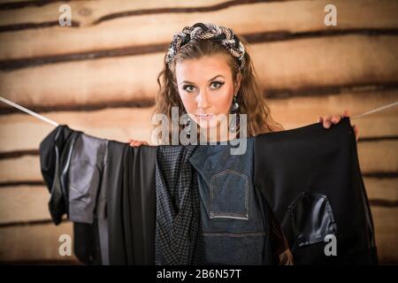 Schöne Frau wählt die richtige Hose, die an einem Seil im Raum hängt. Das Konzept, Dinge für die gewünschte Veranstaltung aus der garderobe collecti zu wählen Stockfoto