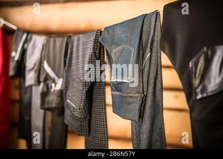 Dunkle, stylische Hosen und Jeans für Damen hängen an einem Seil in der garderobe. Das Konzept, Kleidung für jeden Tag zu wählen. Elegantes Damenbekleidungskonzept Stockfoto