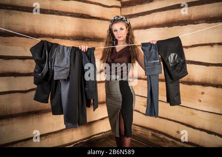 Schöne Frau wählt die richtige Hose, die an einem Seil im Raum hängt. Das Konzept, Dinge für die gewünschte Veranstaltung aus der garderobe collecti zu wählen Stockfoto