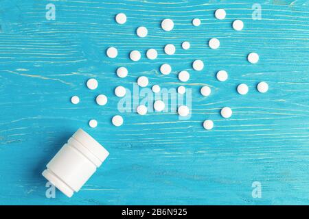 Weiße Pillen wurden aus einem weißen Behälter über blauem Holzhintergrund verschüttet Stockfoto