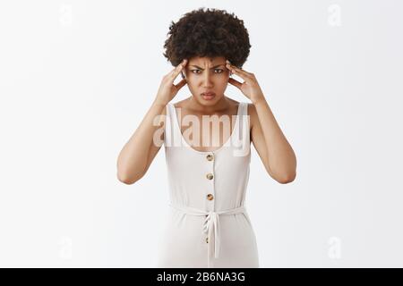 Mein Geist wird von Kopfschmerzen in die Luft sprengen. Intensive aufgeregt afroamerikanische Frau in stilvollen symbolischen Overalls, runzelnd und Hände auf Schläfen halten, während Stockfoto