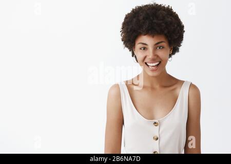 Horizontale Schuss, charmantes, freundliches, stilvolles afrikanische amerikanische Freundin mit Curly Frisur freudig lächelnd und starrte mit höflich und ruhig Stockfoto