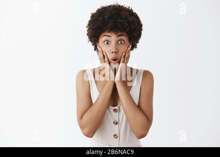 Überrascht attraktive afroamerikanische Frau mit afro Frisur, Schnappatmung Hinterhalt, sehen unglaubliche Giveaway, schauen erstaunt und amüsiert, berühren Stockfoto