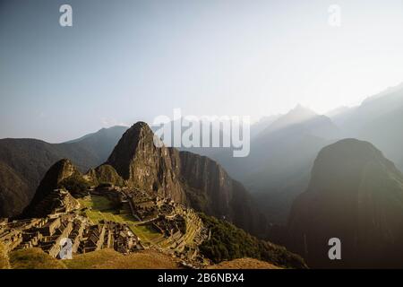 Weltberühmte Inka-Stadt Machu Picchu bei Sonnenaufgang mit gelben Lichtstrahlen und nebligen Wolken (ohne Besucher) (Aguas Calientes, Peru) Stockfoto