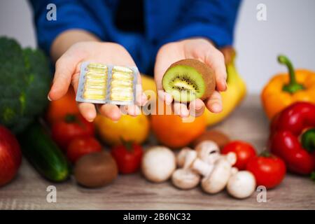 Frau an einem Tisch mit Kiwi und Pillen auf dem Hintergrund von Obst und Gemüse Stockfoto