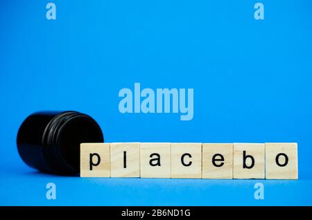 Das Wort PLACEBO auf Holzwürfeln und ein medizinischer dunkler Kolben auf blauem Hintergrund. Stockfoto