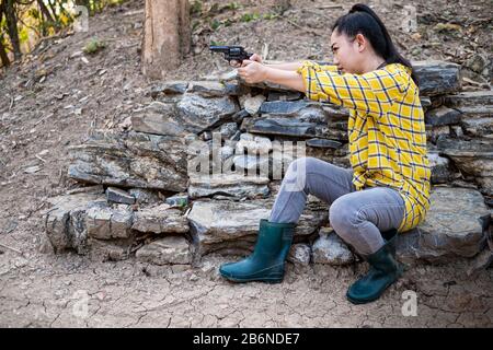 Portrait die Bauer asea Frau, die beim Schuss aus der alten Revolverpistole auf dem Hof einen Stiefel trägt, das Junge Mädchen sitzt in der Haltung des Zieles und Stockfoto