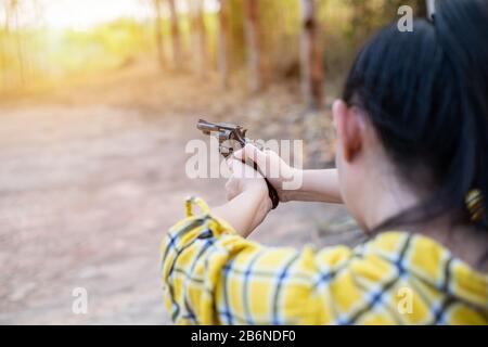 Porträt der Landwirtin asea Woman beim Schuss aus alter Revolverpistole auf dem Hof, Junges Mädchen, das in der Haltung des Zielens und des Auschusses sitzt Stockfoto