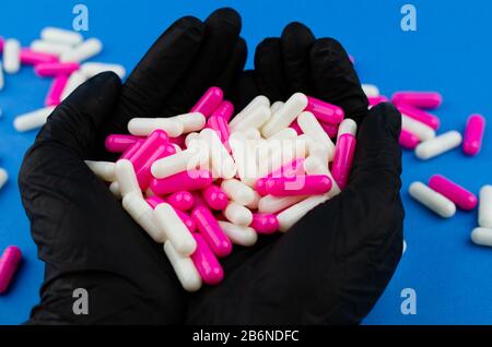 Zwei Hände in schwarzen medizinischen Handschuhen mit einer Handvoll Kapseln oder Medikamenten Stockfoto