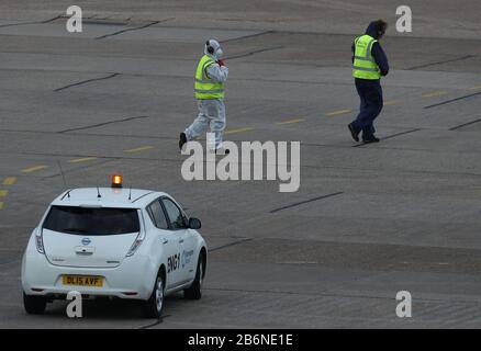 Eine Person, die Schutzkleidung und eine Gesichtsmaske auf der Schürze trägt, als ein Flugzeug, das Passagiere von den Coronavirus-betroffenen Grand Princess Lands auf dem Flughafen Birmingham transportiert, nachdem sie aus den USA zurückgebracht wurden. Stockfoto