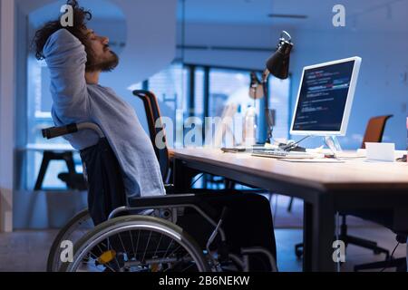 Behinderter Webentwickler im Rollstuhl arbeitet im Büro am Computer, während er im Arbeitsbereich arbeitet. Behinderten- und Behinderungskonzept. Ho Stockfoto