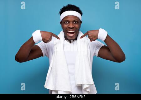 afroamerikanischer selbstbewusster Mann, der nach dem Training mit den Fingern auf sich selbst zeigt, lächelnd vor der Kamera. Studio an blauer Wand gedreht. Stockfoto
