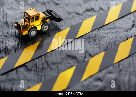 Gelbe Planierraupe auf schwarzem Hintergrund. Schwarzes und gelbes Zaunband vor dem Hintergrund des KONZEPTS. Geschäft, Reparatur, Dienstleistungen. Stockfoto